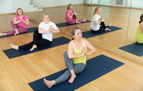 Group of mature active women practicing yoga, making together twisting asanas